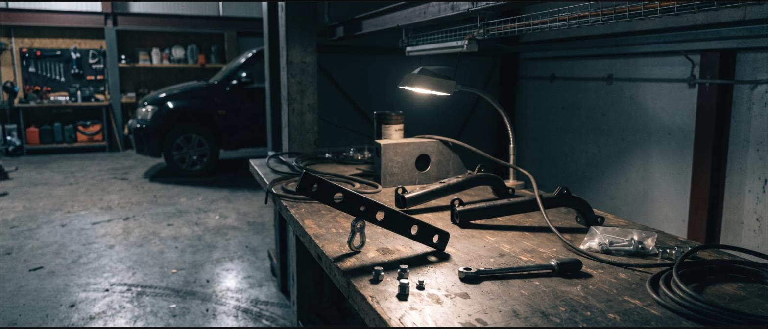 A garage workbench with aftermarket vehicle brackets, bolts and a torque wrench under a lamp